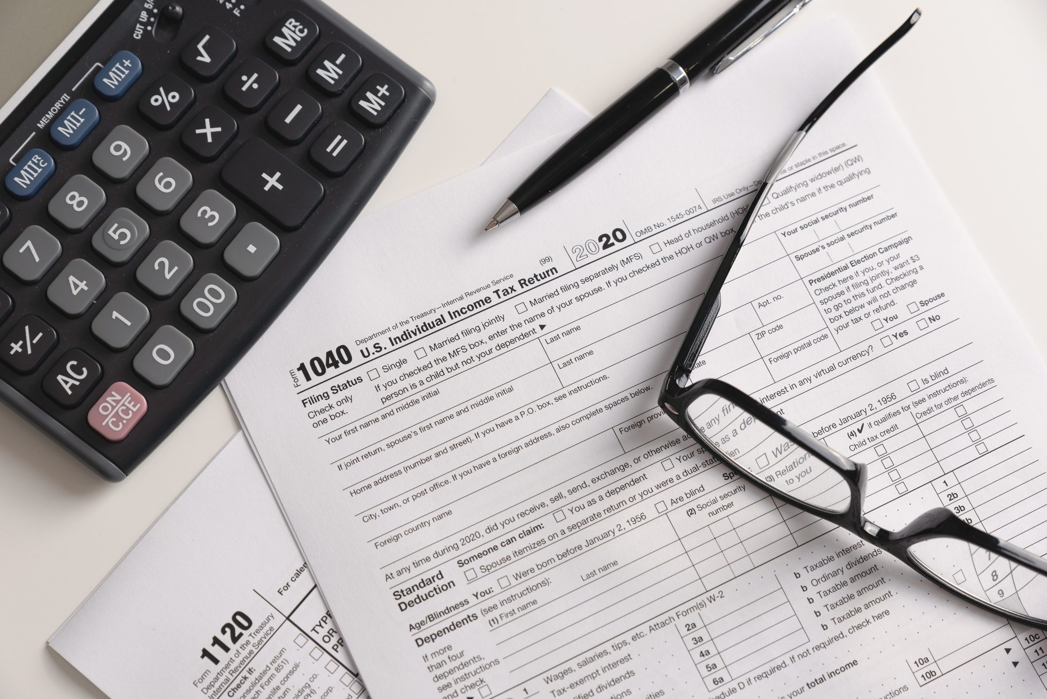US Individual income tax return forms, a pen, calculator, and eyeglasses on a desk.
