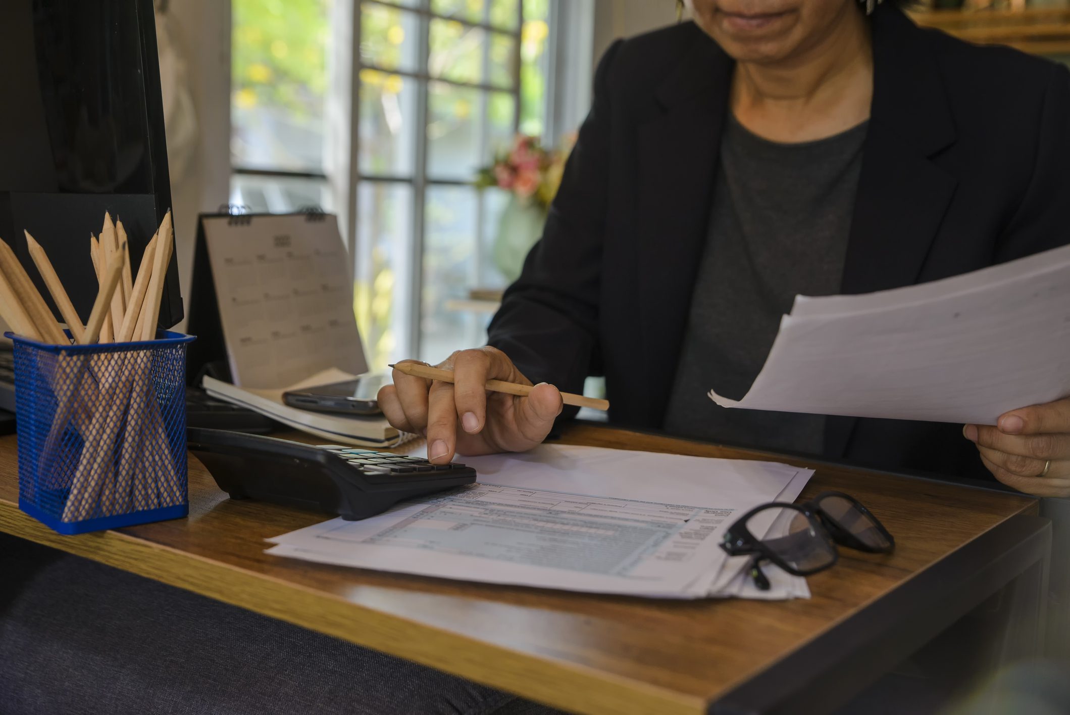 A woman sits at a desk with IRS tax documents in one hand and a calculator in the other hand.